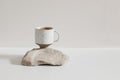 Modern minimal lifestyle still life scene. Speckled ceramic cup of coffee standing on sandstone rock, white table. Beige