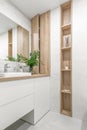 Modern minimalist bathroom interior design with ecru stone tiles and wood wall hidden shelf for bathroom accessories.