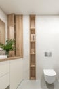Modern minimalist bathroom interior design with ecru stone tiles and wood wall hidden shelf for bathroom accessories.