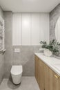 Modern minimalist bathroom interior design with wooden furniture, grey stone tiles, round mirror.