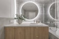 Modern minimalist bathroom interior design with wooden furniture, grey stone tiles, round mirror. Royalty Free Stock Photo