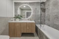 Modern minimalist bathroom interior design with wooden furniture, grey stone tiles, round mirror. Royalty Free Stock Photo