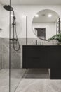 Modern minimalistic bathroom interior design with grey stone tiles, black furniture, eucalyptus in glass vase, round mirror. Royalty Free Stock Photo