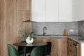 Modern minimalistic kitchen and dining room interior with wooden and white surfaces, green chairs and eucalyptus in ceramic vase. Royalty Free Stock Photo