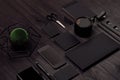 Modern minimalistic work space with black blank stationery, coffee, green plant, phone on black wooden board, top view, inclined.