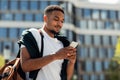 Modern mobile communication. Portrait of black stylish guy using smartphone outdoors, walking in urban city area Royalty Free Stock Photo