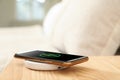 Modern mobile phone charging on wireless pad in bedroom, closeup Royalty Free Stock Photo