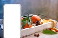 Modern mobile phone with screen, glass of hot tea on tray, delicious vitamin tangerines with leaves, cinnamon sticks, pine cones,