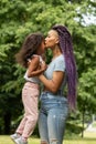 Modern mother, african young woman with braids kisses her daughter, a parent holds a child in her arms in the summer in the park Royalty Free Stock Photo