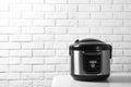 Modern multi cooker on table against brick wall.