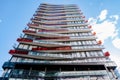 A modern multi-story building with staggered balconies featuring vibrant red accents, set against a clear sky with wispy Royalty Free Stock Photo