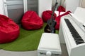 Modern music-room, with white piano and black guitar; red beanbags in the background