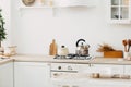 Modern new bright kitchen interior with white furniture and a dining table. gas stove with kettle and pan Royalty Free Stock Photo