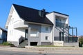 Modern newly built family house with porch and balcony in front surrounded with stone wall and grass next to paved road