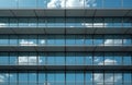 Modern office building facade features glass windows reflecting blue sky, white clouds. Horizontal blinds add texture, pattern. Royalty Free Stock Photo