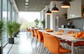 Modern office kitchen break area with orange chairs and table. Bright space with large windows and plants. Contemporary interior Royalty Free Stock Photo