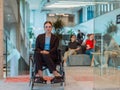 In a modern office, a young businesswoman in a wheelchair is surrounded by her supportive colleagues, embodying the