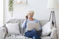 Modern old lady holding laptop and talking by phone Royalty Free Stock Photo