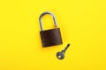 Modern padlock with key on yellow background, flat lay