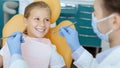 Doctor in protective mask, white coat and rubber gloves with tools examines small smiling kid in chair Royalty Free Stock Photo