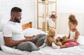 Busy african man browsing on tablet, sad little girl playing with toys alone Royalty Free Stock Photo