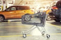Modern plastic empty shopping cart left at roofed underground parking of shopping mall. Supermarket trolley with blurred parked