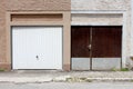 Modern plastic white garage doors on renovated attached family house next to old dilapidated wooden garage doors with metal rain Royalty Free Stock Photo
