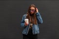 Modern pretty young hipster woman in fashionable denim blue jacket in trendy purple glasses with cup of hot coffee is standing Royalty Free Stock Photo
