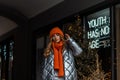 Modern pretty young woman with red hair in a trendy knitted hat with a vintage orange scarf in a youth fashionable shiny silver