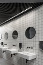 Modern public restroom minimal interior with metro style white tiles, round mirrors, black ceiling.