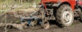 Modern red tractor machinery plowing agricultural field meadow at farm at spring autumn. Farmer cultivating and make soil tillage