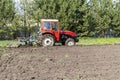 Modern red tractor machinery plowing agricultural field meadow at farm at spring autumn. Farmer cultivating and make soil tillage