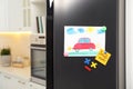 Refrigerator with child`s drawing, note and magnets in kitchen