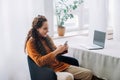 Modern Remote Worker: Happy Young Woman Using Smartphone and Laptop for E-learning and Remote Work at Home. Multi-tasking Young Royalty Free Stock Photo