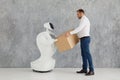 Modern Robotic Technologies. A man communicates with a robot, with cardboard box in hand. delivery concept. Royalty Free Stock Photo