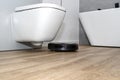 A modern robotic vacuum cleaner cleans the ceramic tiles in the bathroom next to the toilet, an autonomous cleaning rob