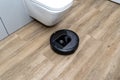 A modern robotic vacuum cleaner cleans the ceramic tiles in the bathroom next to the toilet, an autonomous cleaning robot.