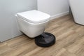 A modern robotic vacuum cleaner cleans the ceramic tiles in the bathroom next to the toilet, an autonomous cleaning robot.