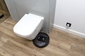 A modern robotic vacuum cleaner cleans the ceramic tiles in the bathroom next to the toilet, an autonomous cleaning robot.