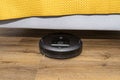 A modern robotic vacuum cleaner cleans the vinyl panels under the bed in bedroom, an autonomous cleaning robot.