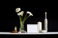 picture frame mockup. Shelf against black wall with decorative candle, glass, wood and rocks. Home plant calla in vase Royalty Free Stock Photo