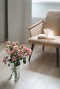 Modern room interior with armchair, book and fresh roses on table. Interior of beautiful living room decorated with flowers Royalty Free Stock Photo