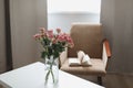 Modern room interior with armchair, book and fresh roses on table. Interior of beautiful living room decorated with flowers Royalty Free Stock Photo