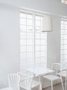 Modern round light lamp cylindrical shape hanging from ceiling over empty table and chairs near tall window.