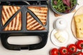 Modern sandwich maker with bread slices and different products on white wooden table, flat lay Royalty Free Stock Photo