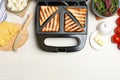Modern sandwich maker with bread slices and different products on white wooden table, flat lay. Space for text Royalty Free Stock Photo