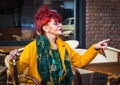 Fashionable woman in age sits in terrace of cafe and points with finger-modern lifestyle of pensionary, vacation or free time