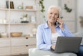 Modern senior woman using laptop and talking on cellphone at home Royalty Free Stock Photo