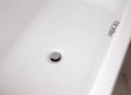 Modern silver drain plug in a new bathroom, water droplets on the walls of the bathtub. Copy space for text Royalty Free Stock Photo
