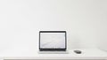 Modern silver laptop and black wireless mouse on a clean white desk against a plain white wall backdrop Royalty Free Stock Photo